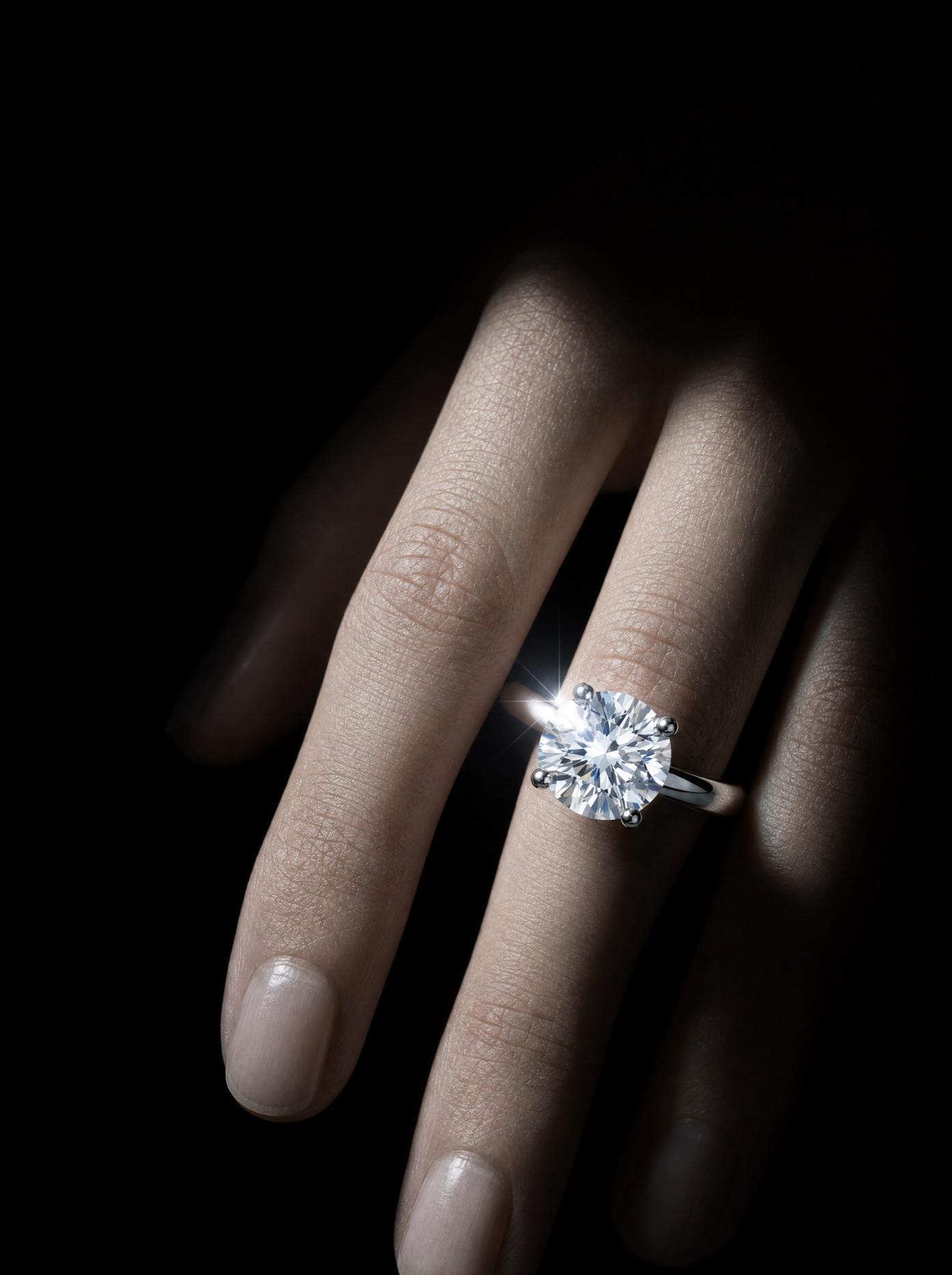 A hand emerging from shadow, the platinum solitaire catching a shaft of light